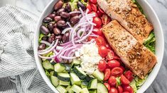 a salad with salmon, tomatoes, cucumber, olives and red onion