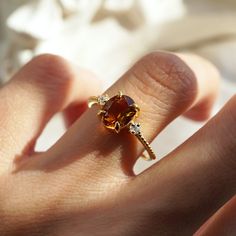 a close up of a person's hand wearing a ring with an orange stone