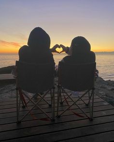 two people sitting in lawn chairs making a heart shape with their hands at the beach