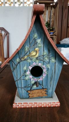 a birdhouse painted with flowers and birds on it's roof is sitting on a table