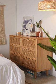 a bedroom with a bed, plant and pictures on the dresser in front of it