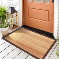 a wooden door mat on the front porch next to a potted plant and lantern