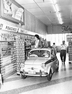 an old black and white photo of people shopping in a store with a small car