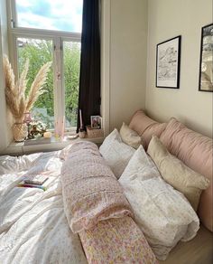 an unmade bed in front of a window with lots of pillows and blankets on it