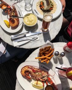 two plates with lobsters and fries are on the table next to some beer glasses