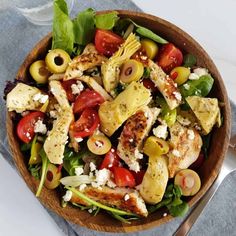 a salad with chicken, olives and tomatoes in a wooden bowl