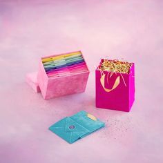 an open pink paper bag with colored pencils in it next to a blue envelope