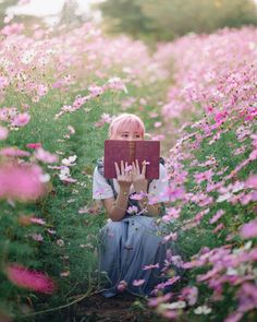 a woman sitting in the middle of a flower field holding up her hands with both hands