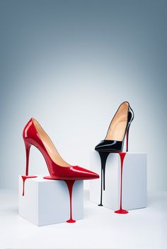 two pairs of red and black high heeled shoes on white blocks, one with dripping paint