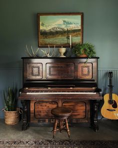 an old piano in a living room next to a potted plant and guitar on the floor