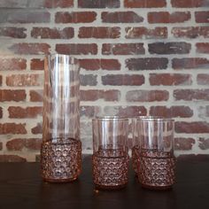 three glasses sitting on top of a table next to a vase and brick wall in the background