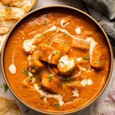 a bowl filled with red curry next to bread and pita bread on the side