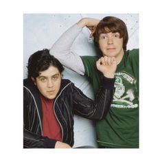 two young men posing for a photo in front of a white wall and one is wearing a green shirt