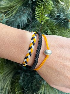 a woman's arm with two bracelets on it and a pine tree in the background