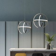 two circular lights hanging from the ceiling above a table with chairs and vases on it