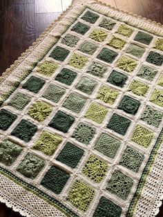 a green and white crocheted blanket sitting on top of a wooden floor