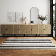 a room with a rug, mirror and two vases on the sideboard next to it