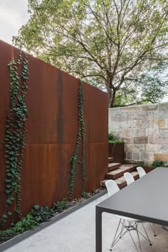 an outdoor dining table and chairs in front of a wall with vines growing on it