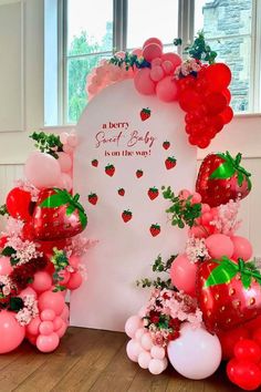 a strawberry themed baby shower is on the way with balloons and streamers in front of it