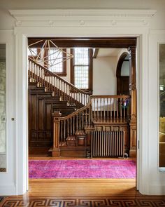 an open door leading to a foyer with pink rug on the floor and wooden stairs