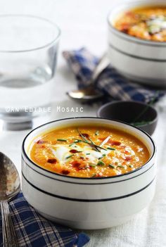 two bowls filled with soup on top of a table next to spoons and glasses