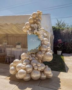 a table topped with lots of balloons next to a white tent covered in tables and chairs