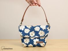 a hand holding a blue and white flowered purse on top of a wooden table