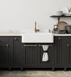 a kitchen with black cabinets and white counter tops, gold pulls on the faucet