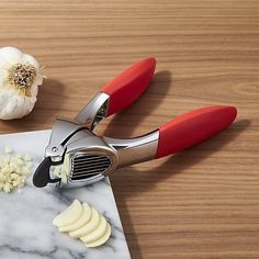 a pair of red handled vegetable cutters on top of a cutting board next to garlic