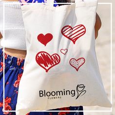 a woman carrying a shopping bag with two hearts on it and the words blooming flowers