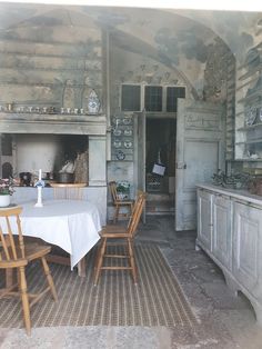 an old fashioned kitchen and dining room with white table cloths on the table, wood chairs