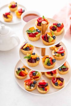 a white plate topped with mini fruit tarts and cupcakes next to a tea pot