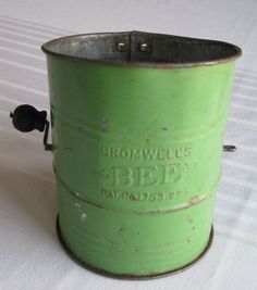 an old green metal bucket sitting on top of a white tablecloth covered bedding