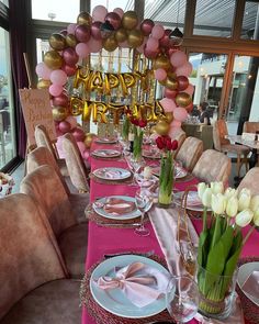 a table set for a birthday party with balloons and flowers