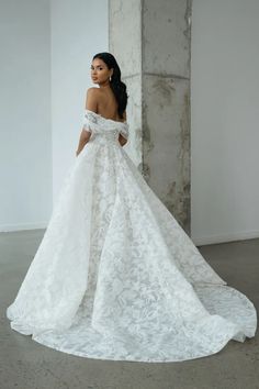 a woman in a white wedding dress standing next to a pillar with her back turned towards the camera