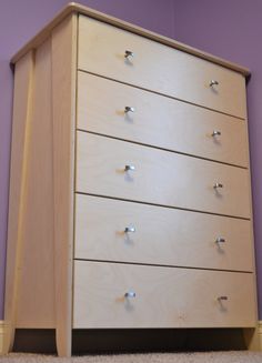 a wooden chest of drawers sitting on top of a carpeted floor next to a purple wall