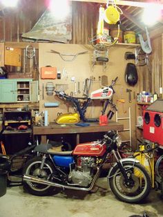 two motorcycles are parked in a garage with lights on the wall and other tools hanging from the ceiling