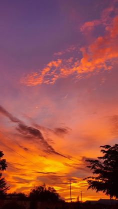 an orange and purple sunset with clouds in the sky over some trees on a street