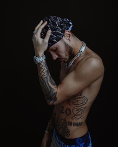 a shirtless man with tattoos on his chest and hands to his face, holding his head