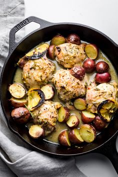 chicken and potatoes in a skillet on top of a white table with a napkin