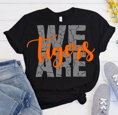 we tigers t - shirt with orange and gray letters on it next to jeans and flowers