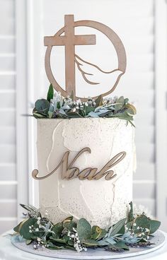 a white cake with greenery and a wooden cross on top