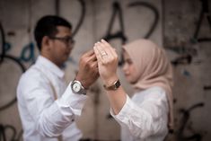 a man and woman standing next to each other with their hands together in front of graffiti covered wall