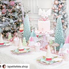 a table topped with lots of colorful cakes and desserts next to a christmas tree