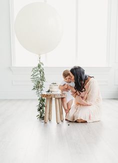 a mother and her daughter sitting on the floor in front of a table with a cake