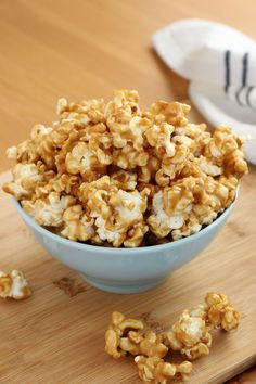 a blue bowl filled with caramel popcorn on top of a wooden cutting board