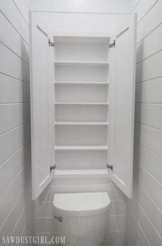 a white toilet sitting inside of a bathroom next to a shelf filled with shelves on the wall