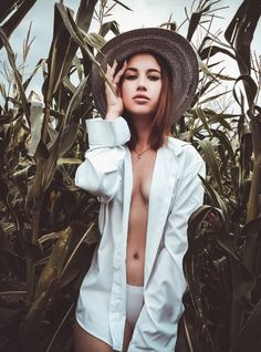 a woman wearing a hat standing in the middle of a cornfield with her hands on her head