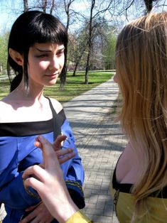 two young women standing next to each other on a brick walkway in a park with trees and grass behind them