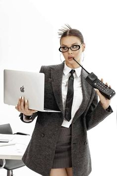 a woman in business attire holding a laptop and cell phone with her mouth wide open